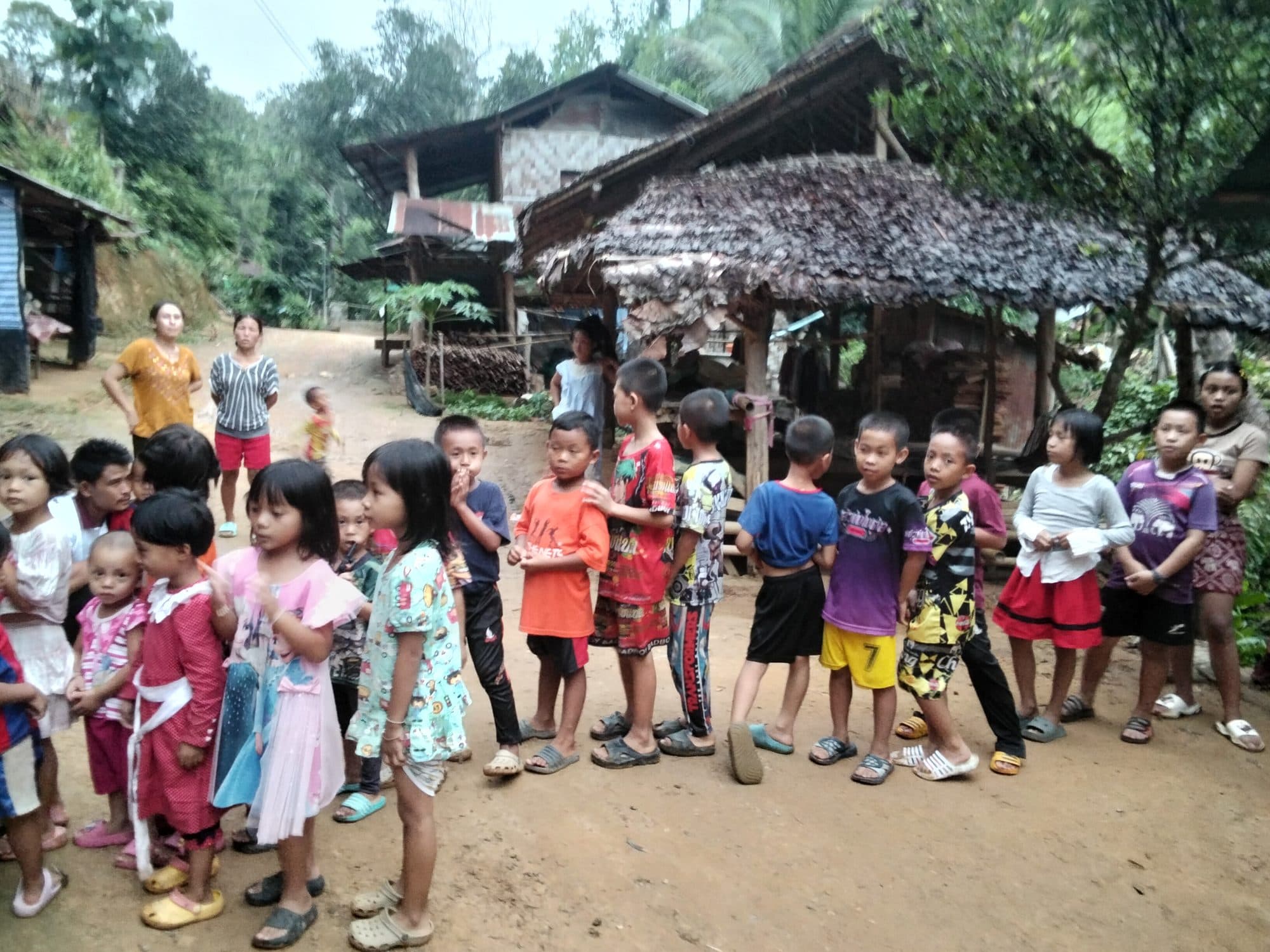 Children of the village lined up together on open ground by their homes.